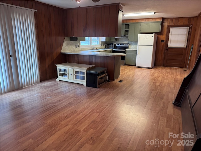 kitchen with stainless steel appliances, kitchen peninsula, a textured ceiling, decorative backsplash, and light wood-type flooring