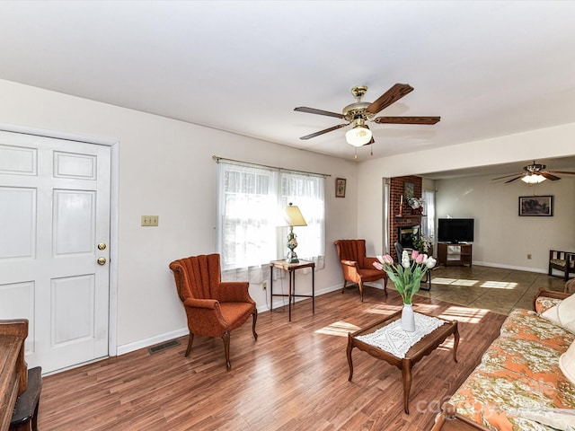 living area featuring a fireplace, visible vents, a ceiling fan, wood finished floors, and baseboards