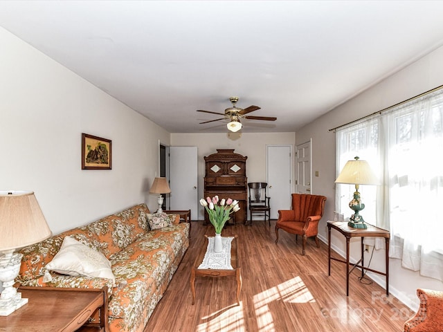 living area featuring wood finished floors, a ceiling fan, and baseboards