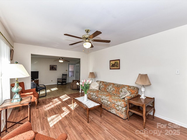 living area featuring a ceiling fan, baseboards, and wood finished floors