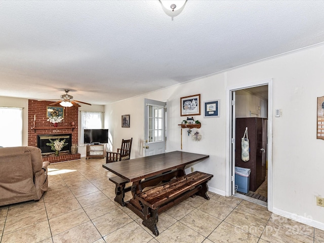 dining room featuring a brick fireplace, light tile patterned floors, a ceiling fan, and a textured ceiling