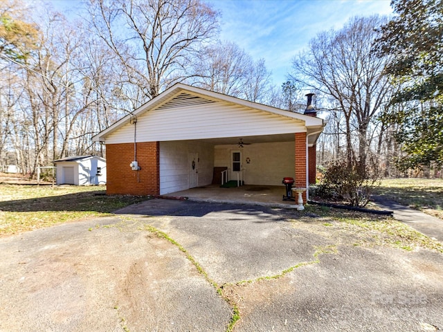 view of side of home featuring driveway, ceiling fan, an outbuilding, a shed, and brick siding