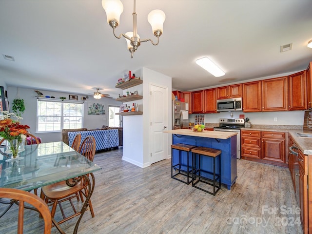 kitchen with light wood-type flooring, pendant lighting, ceiling fan with notable chandelier, and appliances with stainless steel finishes