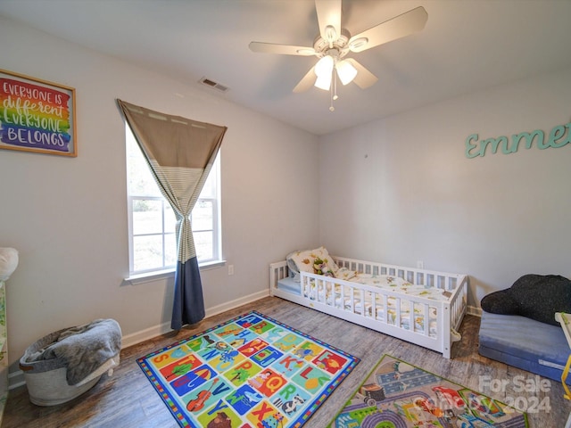 bedroom featuring ceiling fan, hardwood / wood-style floors, and a crib