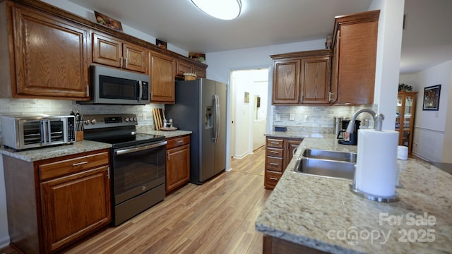 kitchen featuring decorative backsplash, appliances with stainless steel finishes, light wood-type flooring, and light stone countertops