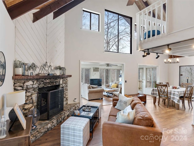 living room with hardwood / wood-style flooring, beam ceiling, a stone fireplace, and high vaulted ceiling