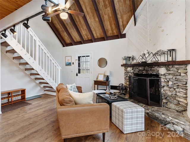 living room featuring ceiling fan, high vaulted ceiling, beamed ceiling, a fireplace, and light hardwood / wood-style floors