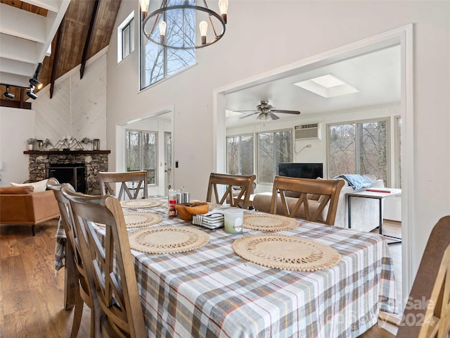 dining area with a stone fireplace, high vaulted ceiling, beamed ceiling, hardwood / wood-style floors, and ceiling fan with notable chandelier