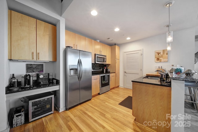 kitchen with light brown cabinets, sink, hanging light fixtures, light wood-type flooring, and stainless steel appliances