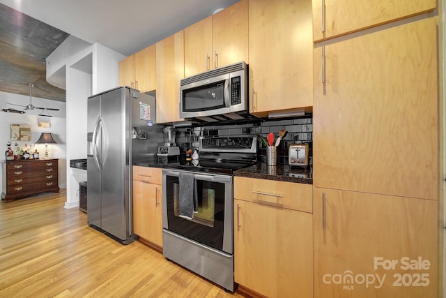 kitchen with light brown cabinets, backsplash, dark stone countertops, appliances with stainless steel finishes, and light hardwood / wood-style floors