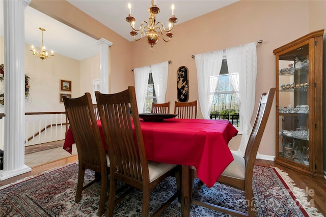 dining space with hardwood / wood-style floors, decorative columns, and a notable chandelier