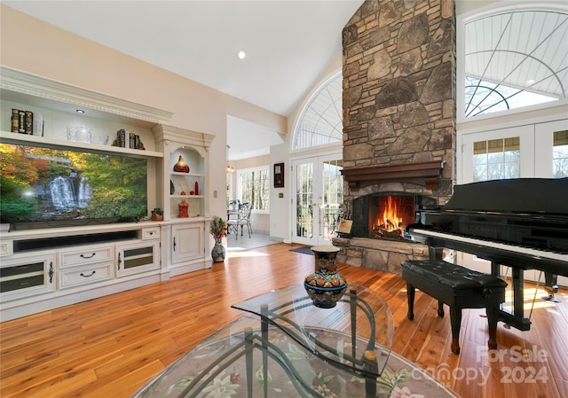 living room featuring a stone fireplace, high vaulted ceiling, and light wood-type flooring