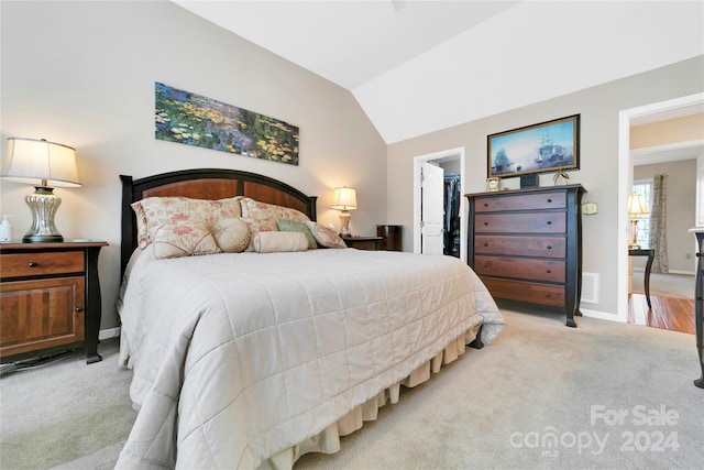 bedroom featuring a walk in closet, light carpet, a closet, and lofted ceiling