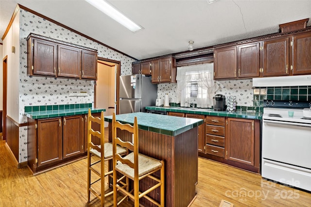 kitchen featuring stainless steel refrigerator, electric range, a breakfast bar, and light hardwood / wood-style floors