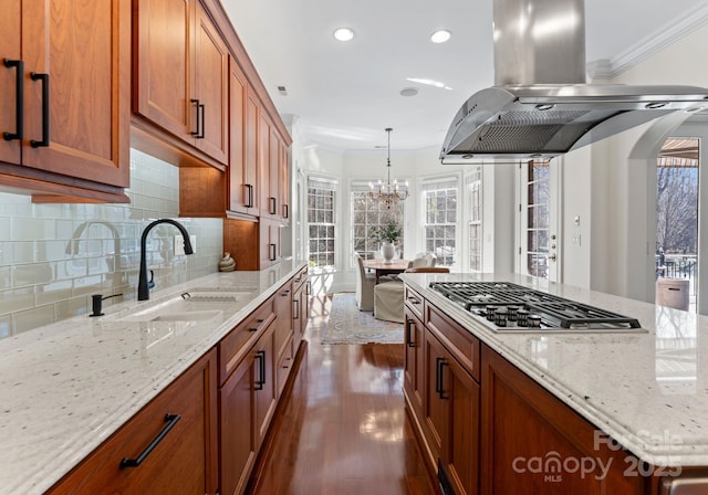 kitchen with pendant lighting, stainless steel gas stovetop, sink, decorative backsplash, and island range hood