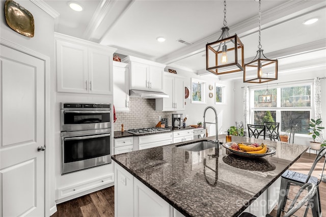 kitchen with beamed ceiling, sink, appliances with stainless steel finishes, and an island with sink