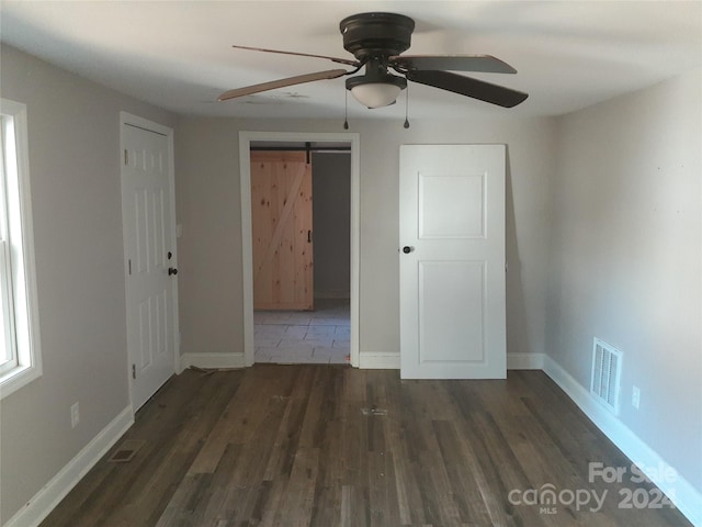 unfurnished bedroom featuring dark hardwood / wood-style flooring, a barn door, and ceiling fan