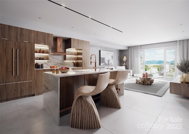 kitchen featuring wall chimney range hood, a breakfast bar, a mountain view, decorative backsplash, and a kitchen island with sink