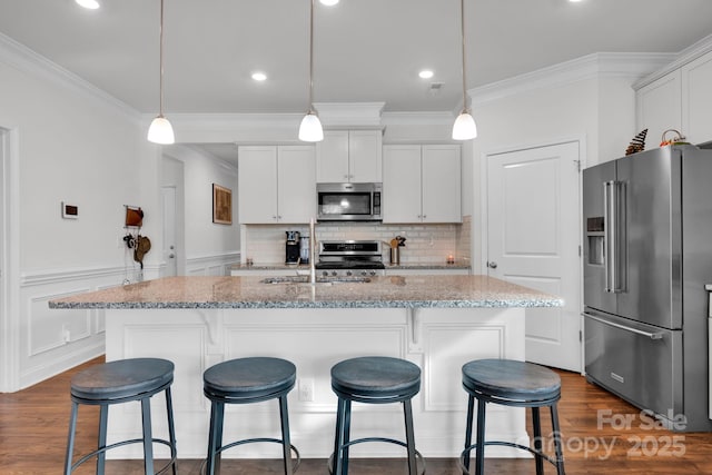 kitchen with light stone countertops, appliances with stainless steel finishes, white cabinetry, and a kitchen island with sink