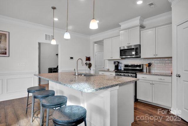 kitchen with sink, hanging light fixtures, light stone counters, an island with sink, and appliances with stainless steel finishes