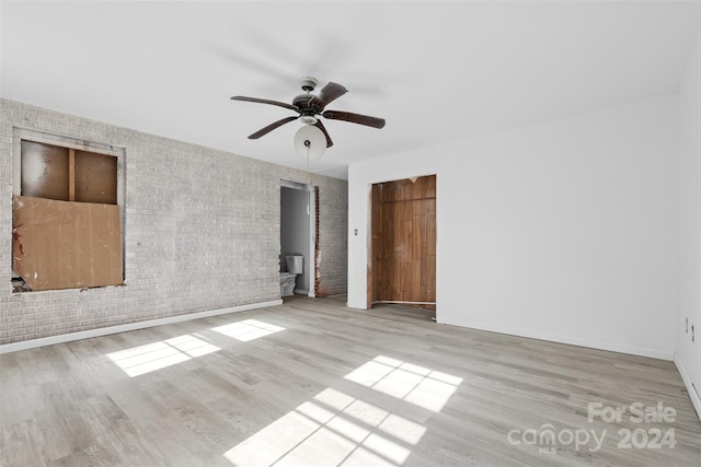 unfurnished room featuring ceiling fan, light hardwood / wood-style floors, and brick wall