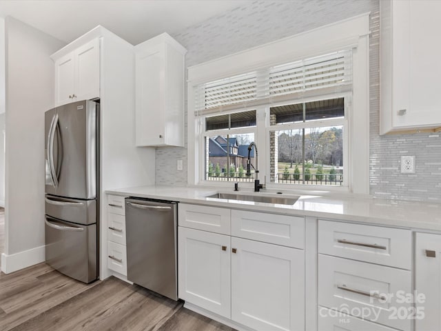 kitchen featuring backsplash, sink, light hardwood / wood-style flooring, appliances with stainless steel finishes, and white cabinetry