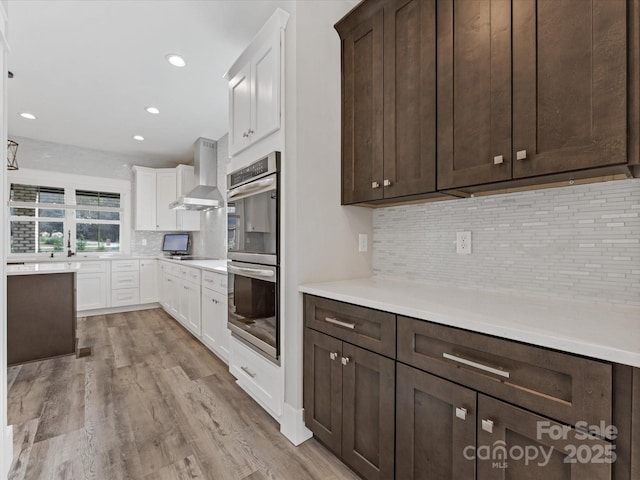 kitchen featuring backsplash, stainless steel appliances, wall chimney range hood, light hardwood / wood-style flooring, and white cabinetry