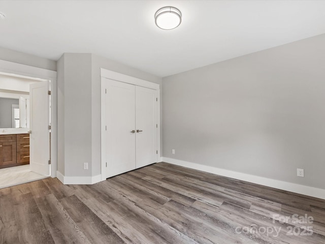 unfurnished bedroom with hardwood / wood-style floors, ensuite bath, and a closet