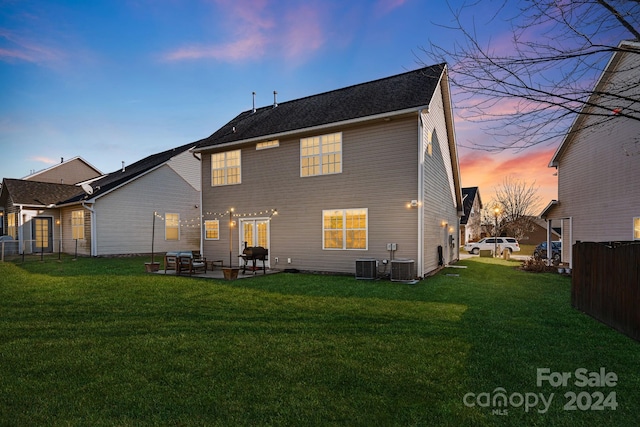 back house at dusk featuring a lawn, central air condition unit, and a patio