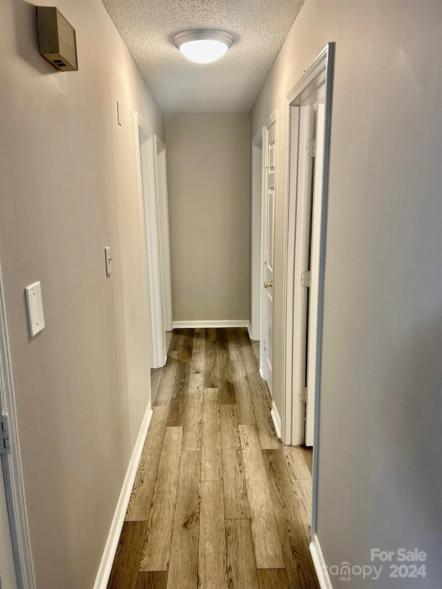 hall with a textured ceiling and light hardwood / wood-style floors