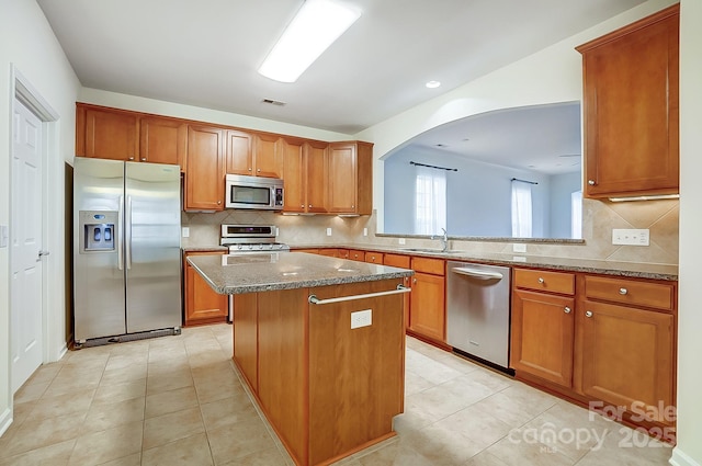 kitchen with light stone counters, stainless steel appliances, sink, a kitchen island, and light tile patterned flooring