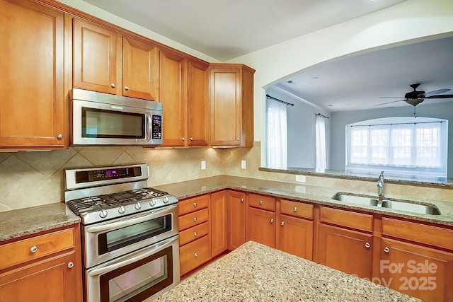 kitchen featuring appliances with stainless steel finishes, backsplash, light stone counters, ceiling fan, and sink