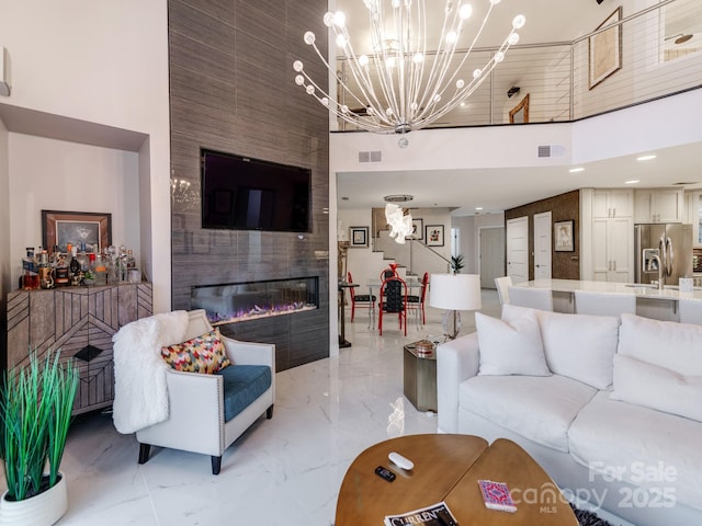 living room featuring a high ceiling, a notable chandelier, sink, and a large fireplace