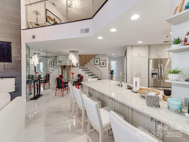 kitchen featuring light stone countertops, a breakfast bar, stainless steel refrigerator with ice dispenser, a towering ceiling, and sink