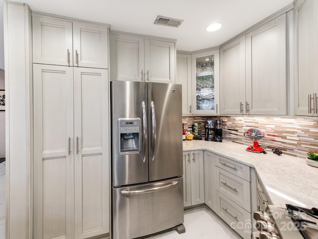 kitchen with light stone counters, stainless steel fridge with ice dispenser, backsplash, and gray cabinetry