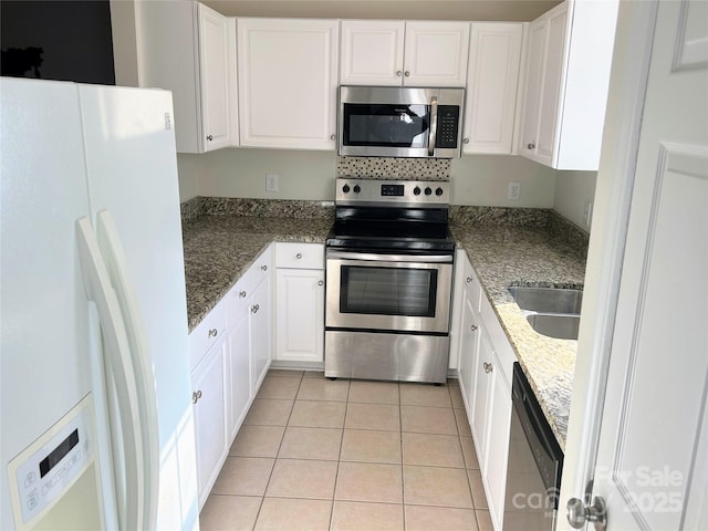 kitchen featuring stainless steel appliances, white cabinetry, light tile patterned floors, and dark stone counters