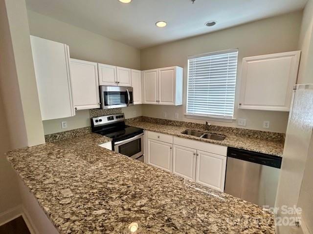 kitchen with sink, white cabinetry, stainless steel appliances, light stone countertops, and kitchen peninsula