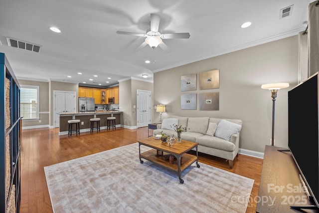 living room featuring ceiling fan, light wood-type flooring, and crown molding