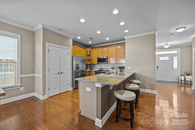 kitchen with kitchen peninsula, light stone countertops, appliances with stainless steel finishes, and ornamental molding