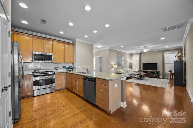 kitchen with light stone counters, kitchen peninsula, appliances with stainless steel finishes, ceiling fan, and sink