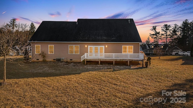 back house at dusk featuring cooling unit, a deck, and a lawn