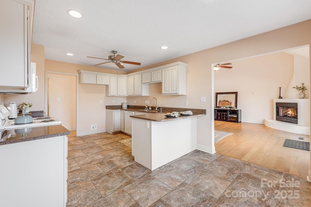 kitchen featuring sink, dark stone countertops, a large fireplace, and kitchen peninsula