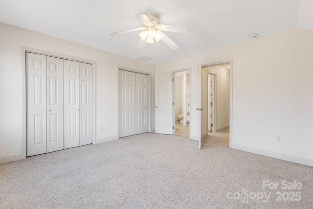 unfurnished bedroom featuring multiple closets, ceiling fan, and light colored carpet