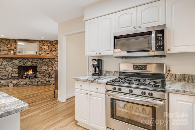 53 Jump Cove Rd, Weaverville, NC 28787 - kitchen featuring appliances with stainless steel finishes, light wood finished floors, white cabinets, light stone countertops, and a fireplace