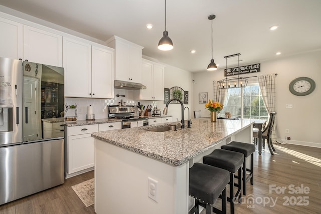 kitchen with white cabinets, appliances with stainless steel finishes, a center island with sink, and sink