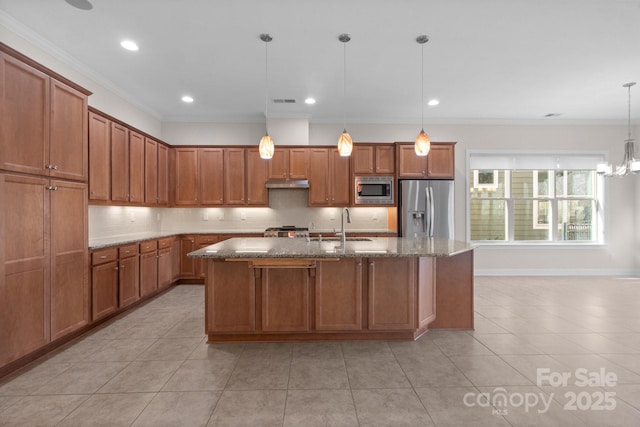 kitchen with a center island with sink, hanging light fixtures, appliances with stainless steel finishes, brown cabinetry, and a sink