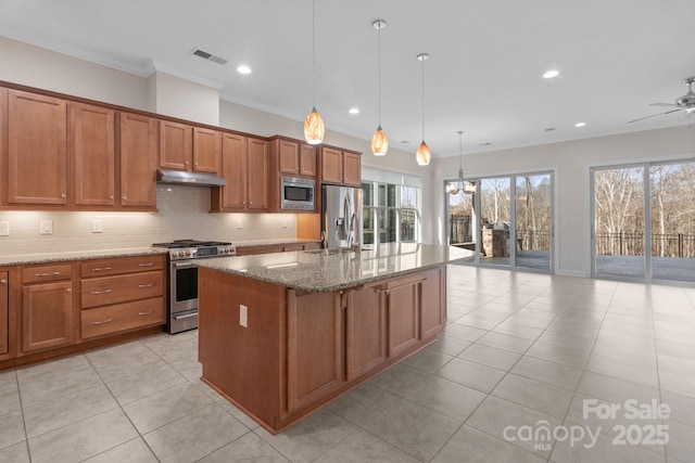 kitchen featuring visible vents, decorative light fixtures, a kitchen island with sink, stainless steel appliances, and under cabinet range hood