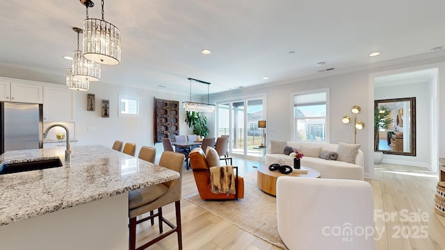 living room with a notable chandelier, crown molding, light wood-type flooring, and sink