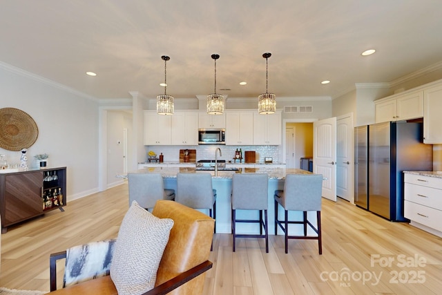 kitchen with light stone countertops, stainless steel appliances, decorative light fixtures, white cabinets, and ornamental molding