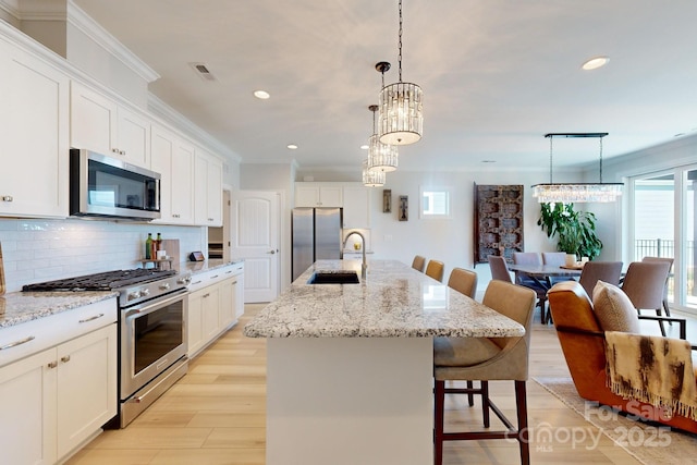 kitchen featuring a center island with sink, sink, appliances with stainless steel finishes, tasteful backsplash, and decorative light fixtures